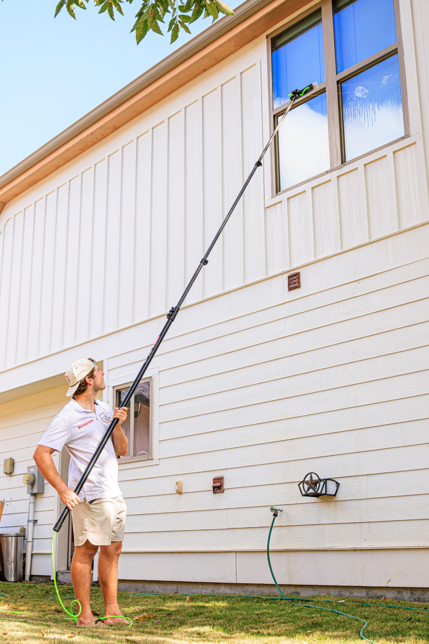 Bellaire Pro Wash technician cleaning second-story windows with a water-fed pole on a Houston home